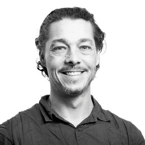 Personne souriante avec une chemise, fond gris clair.